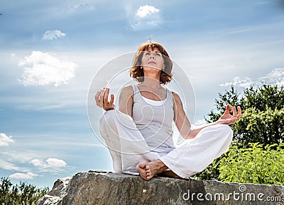 Beautiful 50s woman sitting on a stone in yoga lotus position Stock Photo