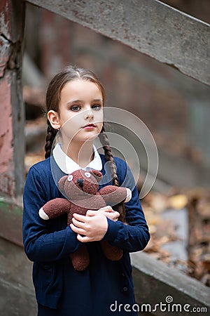 Beautiful sad little girl with with pigtails, dressed in dark blue standing near mystic abandoned building with gothic stairs and Stock Photo