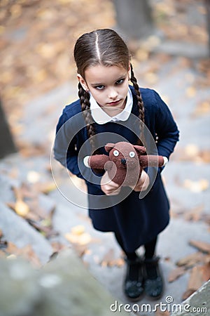 Beautiful sad little girl with with pigtails, dressed in dark blue standing near mystic abandoned building with gothic stairs and Stock Photo