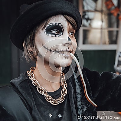 Beautiful scary little girl celebrating halloween, chewing gummy worm. Terrifying face makeup and witch costume Stock Photo