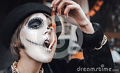 Beautiful scary little girl celebrating halloween, chewing gummy worm. Terrifying face makeup and witch costume Stock Photo