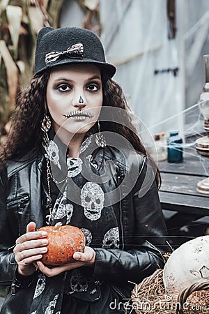 Beautiful scary little girl celebrating halloween. Terrifying black, white half-face makeup and witch costume, stylish image. Stock Photo