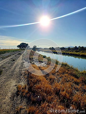 Beautiful scene of water canal and dirt road facing the sunshine Stock Photo