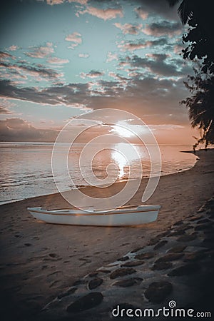 Beautiful scenery of a white rafting boat at the sandy beach of Moorea island during a cloudy sunset Stock Photo
