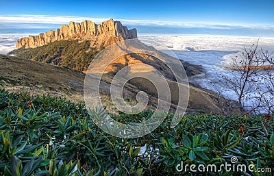 Beautiful scenic autumn landscape of majestic Bolshoy Tkhach rocky mountain peak under blue sky at sunset above white shroud of lo Stock Photo