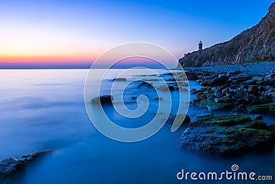 Beautiful seascape with lighthouse at sunset. Mountains and the sea with a long passage. Stock Photo