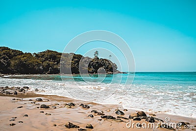 Beautiful secluded beach on an isolated island. Blue water and white waves spume on a sandy beach with stones in Sri Lanka. Escape Stock Photo