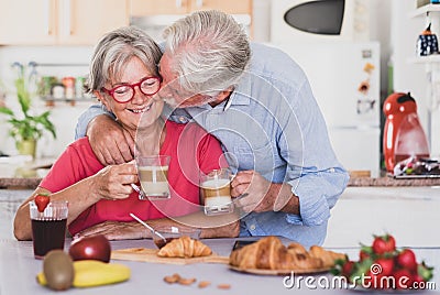 Beautiful senior couple having breakfast at home, starting morning with a kiss. Hot cappuccino in the hands Stock Photo