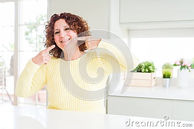 Beautiful senior woman wearing yellow sweater smiling confident showing and pointing with fingers teeth and mouth Stock Photo
