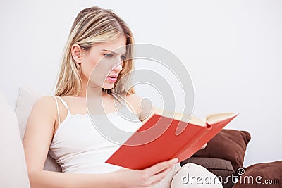 Beautiful serious young woman reading a book, relaxing at home Stock Photo