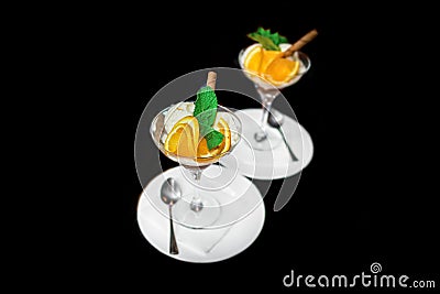 Beautiful serving of scoops of ice cream with slices of orange and mint, ice cream in a glass and saucer with a spoon on a black Stock Photo