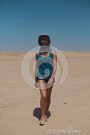 Beautiful blonde girl in helmet and sunglasses wearing in shorts and t-shirt walking across desert Stock Photo