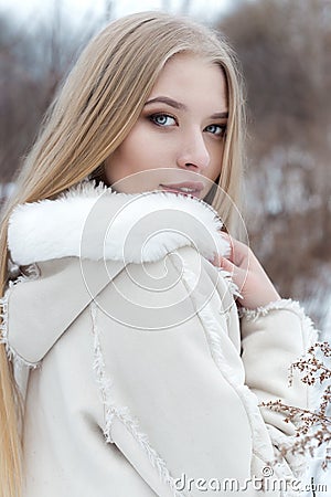 Beautiful blonde girl with long hair, full lips in a white coat walking in the winter woods Stock Photo