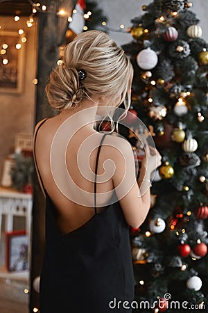 Beautiful and sexy blonde model girl with modish hairstyle in the black dress with nude back decorating the Christmas Stock Photo