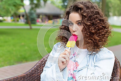 Beautiful cheerful girl with curly hair with full lips bright color eating ice cream in the park in a summer cafe Stock Photo