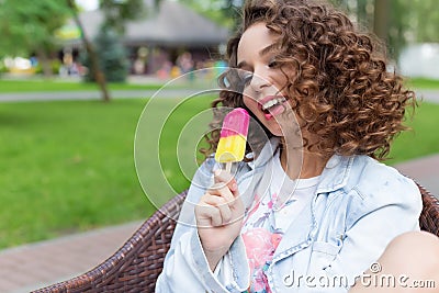 Beautiful cheerful girl with curly hair with full lips bright color eating ice cream in the park in a summer cafe Stock Photo