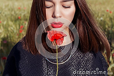 Beautiful cute girl with big lips and red lipstick in a black jacket with a flower poppy standing in a poppy field at sunset Stock Photo