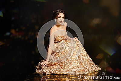Beautiful and glamorous brunette girl in a gold dress. Blac Stock Photo
