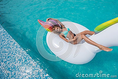 Beautiful slender blonde sitting big inflatable unicorn pool Stock Photo