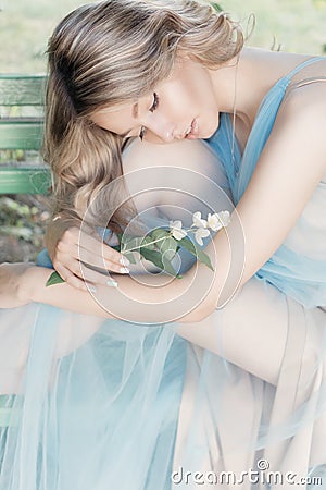 Beautiful tender blonde girl in blue light dress with a sprig of jasmine in his hands sitting the garden in the style Stock Photo
