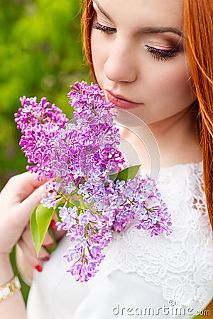 Beautiful woman with fiery red hair in the garden with lilac and white dress with beautiful makeup Stock Photo