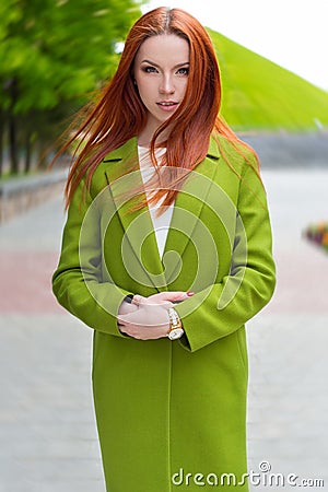 Beautiful woman with fiery red hair with green coat walking through the streets of the city Stock Photo