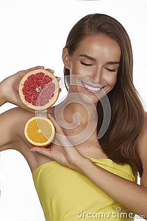 Beautiful young woman with perfect healthy skin and long brown hair day makeup bare shoulders holding orange lemon grapefruit Stock Photo