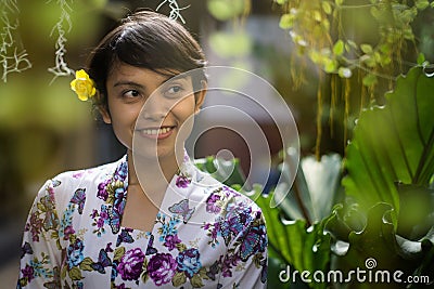 Beautiful short hair Asian Indonesian girl smelling with nature green background. She using floral pattern traditional shirt and a Stock Photo