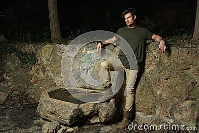 Beautiful shot of athletic male posing confidently next to an old stone source of drinking water Stock Photo