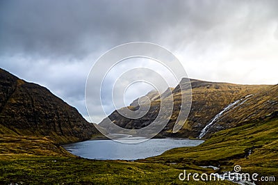 Beautiful shot of a pond surrounded by moutnasin under a cloudy sky on the farce island Stock Photo