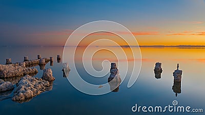 Beautiful shot of stones in the ocean with the reflection of the orange sunset sky in it Stock Photo