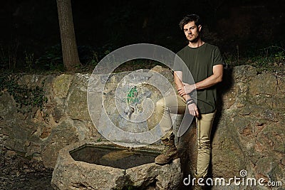 Beautiful shot of young athletic male standing next to old stone source of drinking water Stock Photo