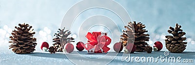 Beautiful simple Christmas banner with copy space. Cute Christmas present, red ornaments and pine cones on shiny blue background. Stock Photo