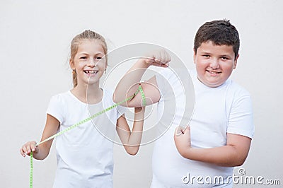 Beautiful skinny small girl measuring smiling big fat boy muscle size by tape Stock Photo