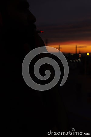 Beautiful sky at sunset with towering towers, against the background of a bearded man smokes Stock Photo