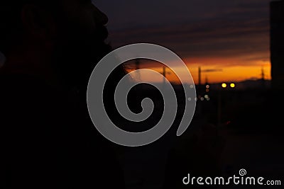 Beautiful sky at sunset with towering towers, against the background of a bearded man smokes Stock Photo