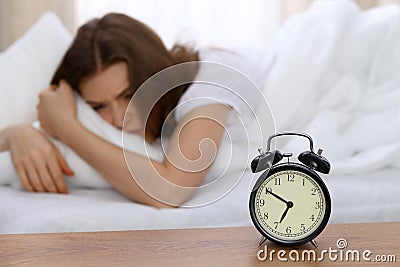 Beautiful sleeping woman lying in bed and trying to wake up with alarm clock. Girl having trouble with getting up early Stock Photo