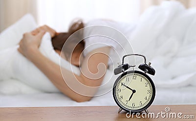 Beautiful sleeping woman lying in bed and trying to wake up with alarm clock. Girl having trouble with getting up early Stock Photo