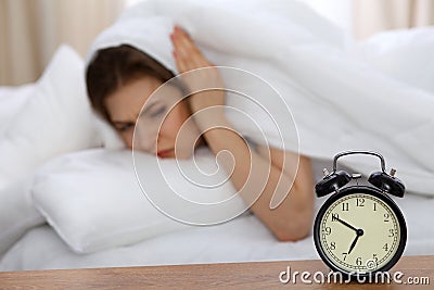 Beautiful sleeping woman lying in bed and trying to wake up with alarm clock. Girl having trouble with getting up early Stock Photo