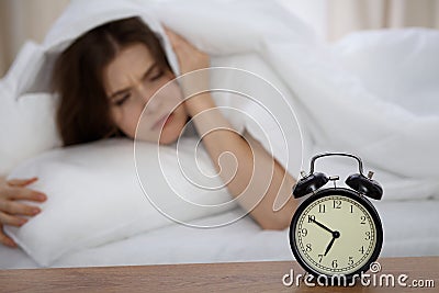 Beautiful sleeping woman lying in bed and trying to wake up with alarm clock. Girl having trouble with getting up early Stock Photo