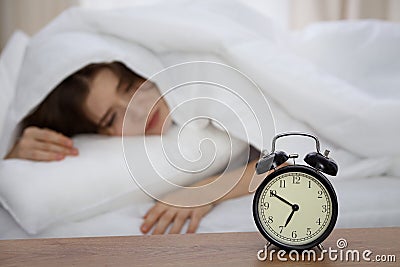 Beautiful sleeping woman lying in bed and trying to wake up with alarm clock. Girl having trouble with getting up early Stock Photo