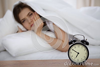 Beautiful sleeping woman lying in bed and trying to wake up with alarm clock. Girl having trouble with getting up early Stock Photo