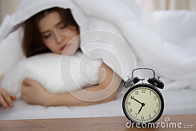 Beautiful sleeping woman lying in bed and trying to wake up with alarm clock. Girl having trouble with getting up early Stock Photo