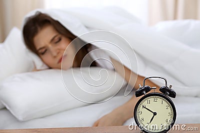 Beautiful sleeping woman lying in bed and trying to wake up with alarm clock. Girl having trouble with getting up early Stock Photo