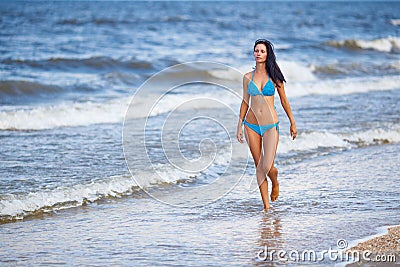 Beautiful slender woman in a blue swimsuit walking on the beach Stock Photo