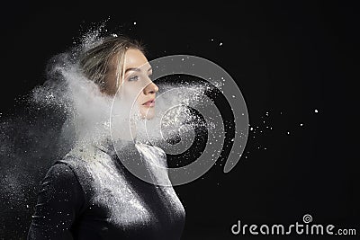 Beautiful slim girl wearing a black gymnastic bodysuit covered with clouds of the flying white powder poses on a dark background. Stock Photo