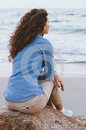 Beautiful slim woman with curly hair sitting on a rock Stock Photo