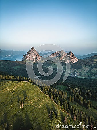 Beautiful small town in green valley on mountainside with field, pine forest and lake in distance Stock Photo