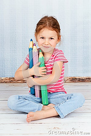 Beautiful smart preschool girl holding big crayons Stock Photo