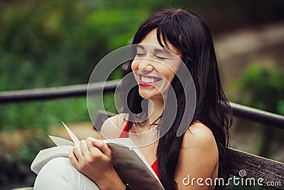 Beautiful smart woman reading a book and laughing in the green park outdoors Stock Photo